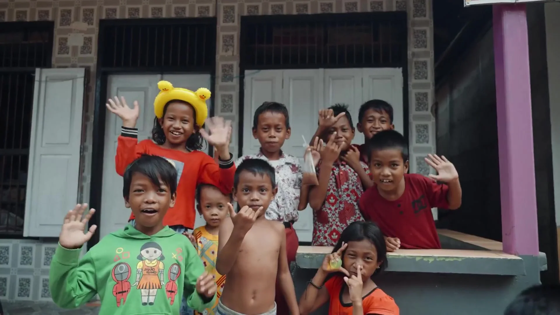 Smiling village children waving and posing in front of a tiled house with white wooden shutters
