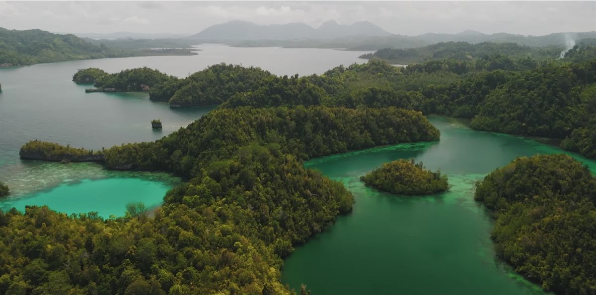 Aerial view of forested islets and turquoise channels with hazy mountains in the distance