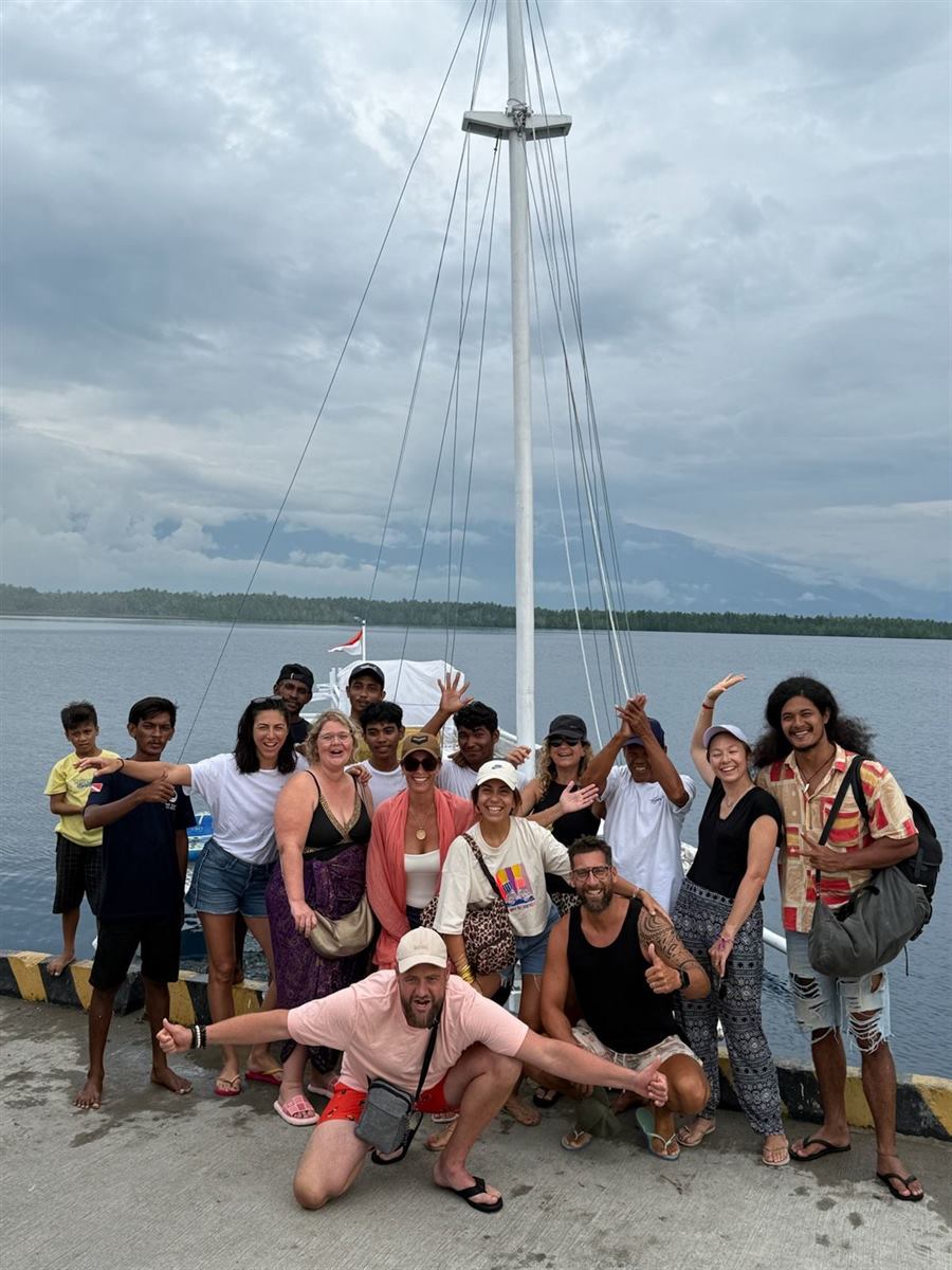 Cheerful group of travellers and locals posing on a concrete pier in front of a boat's tall mast