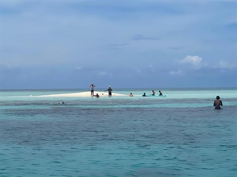 Guests standing on a sandbar surrounded by shallow sea